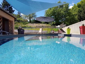 Una piscina con agua azul cristalina, rodeada por una terraza con sillas de descanso y una zona con sombra.