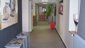 Un pasillo decorado con obras de arte, una planta y mesas con revistas.