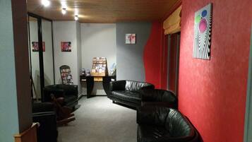 Una habitación con una pared roja, un sofá de cuero negro, un escritorio de madera con una computadora y una estantería.