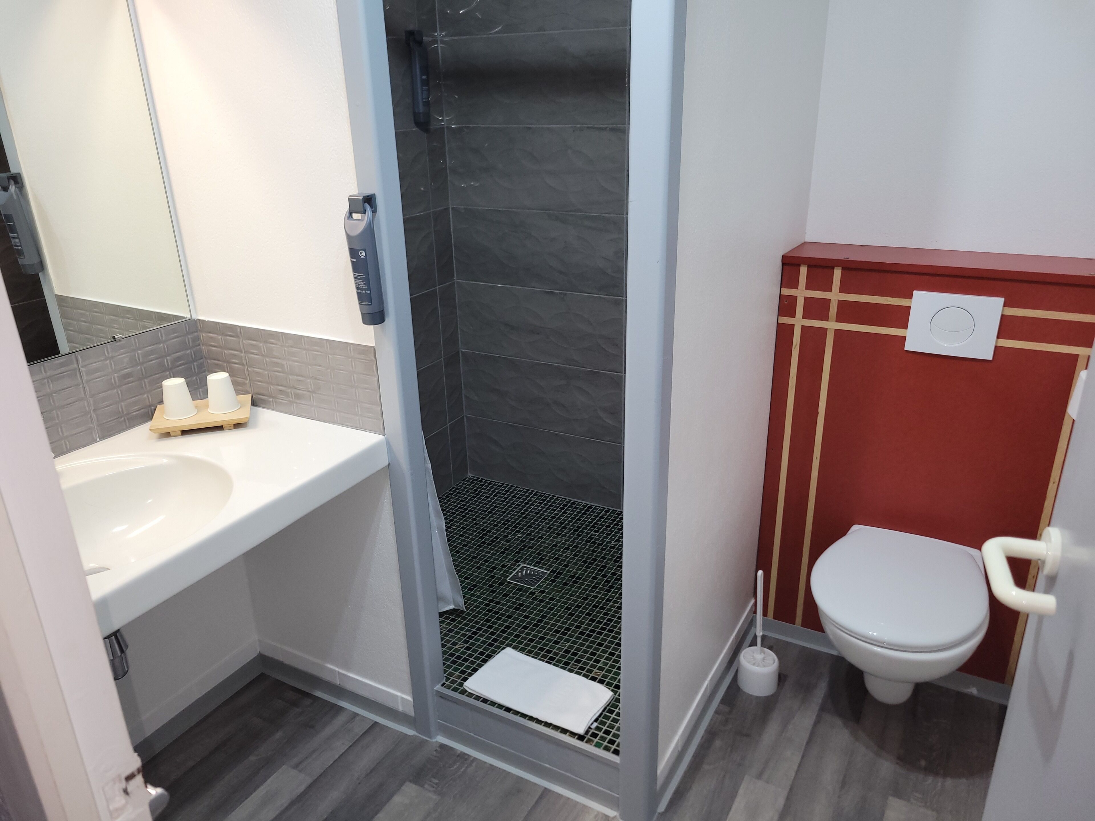 A bathroom with a white sink, a shower with a black tiled wall, and a toilet with a red accent wall.