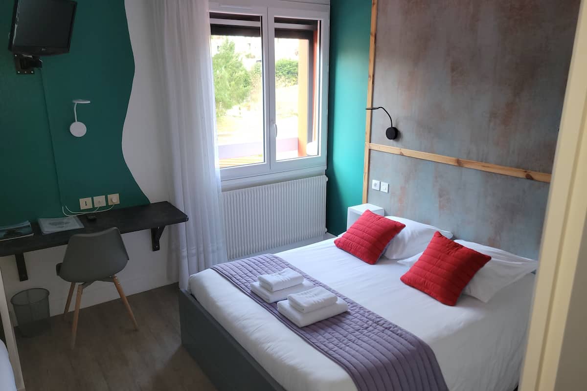A hotel room with a bed, a desk, a chair, a TV, and a window with curtains.