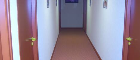 A hallway with carpeted floors, wooden doors, and framed pictures on the walls.