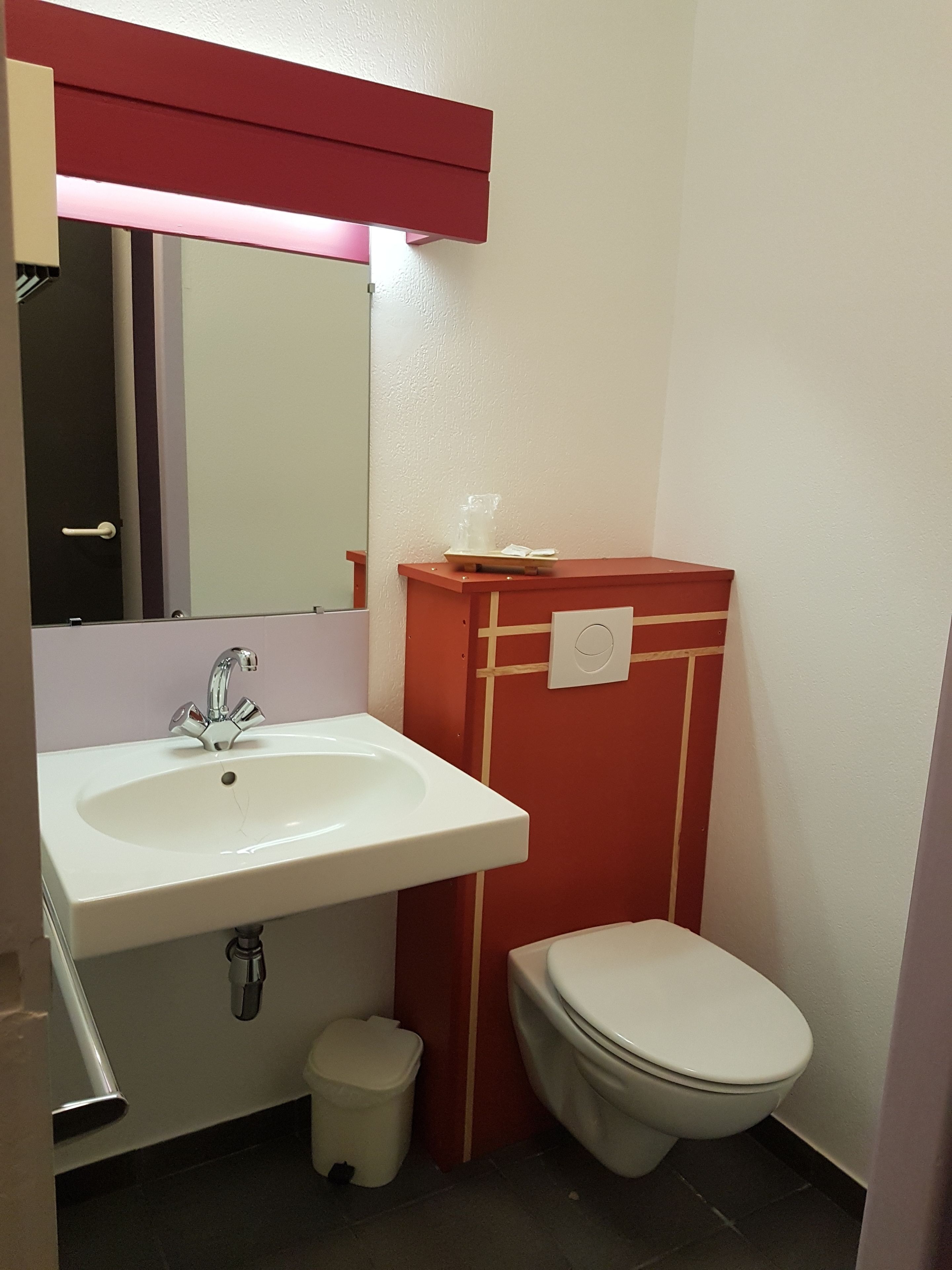 Une salle de bain avec un lavabo blanc, un meuble-lavabo rouge et des toilettes blanches.
