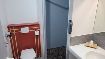 A compact bathroom with a white toilet, a red sink vanity, a shower area, and a small mirror.