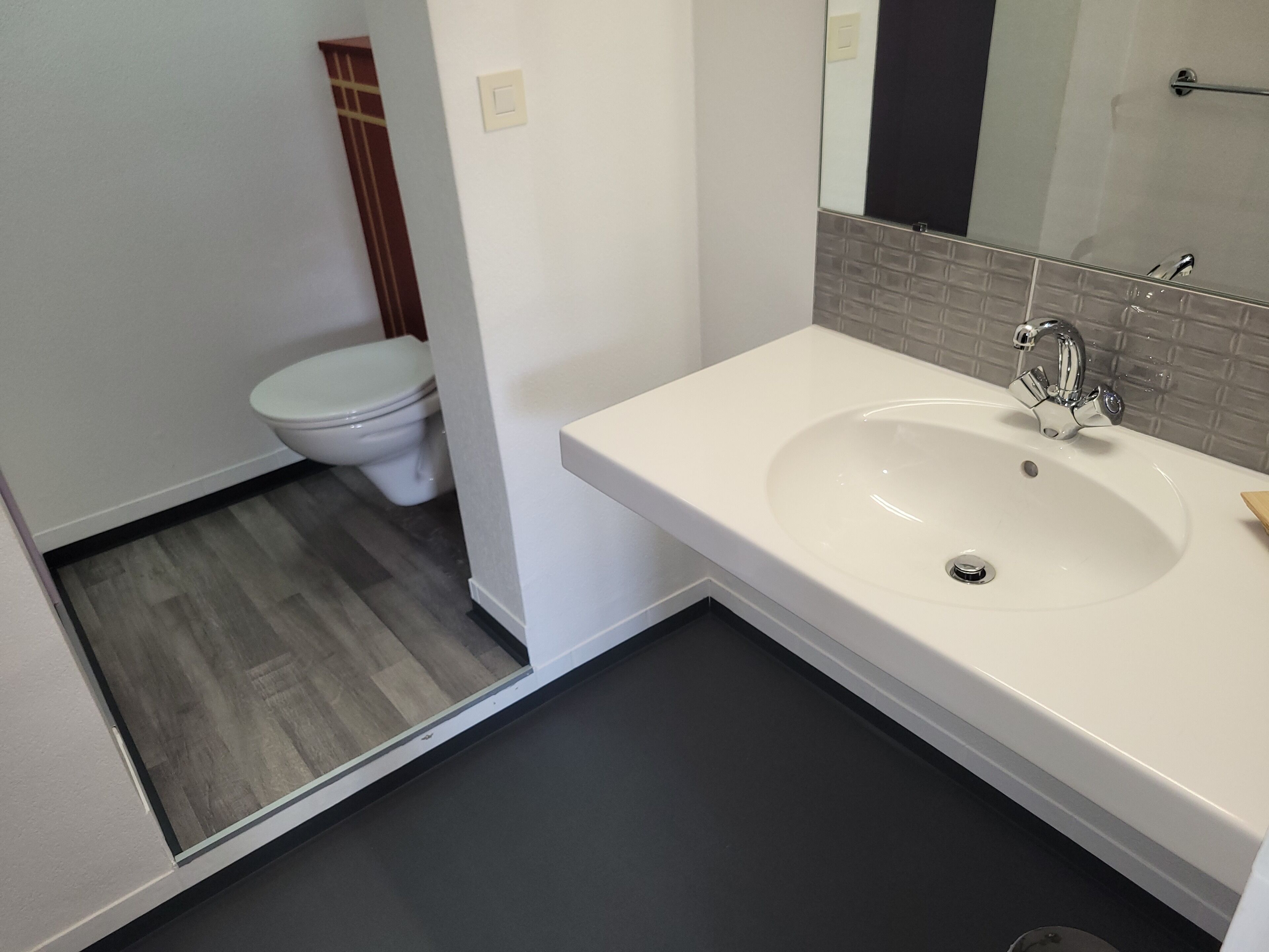 Un baño moderno con lavamanos blanco, espejo e inodoro.