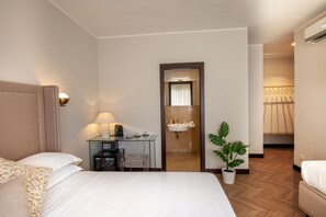 A hotel room with a bed, a desk with a lamp, a potted plant, and a bathroom visible through a door. - Daplace - Hotel Gran Torino Suites (Rome)