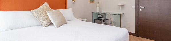 A neatly made bed with white bedding and decorative pillows, a glass side table with a lamp, and a wooden door. - Daplace - Hotel Gran Torino Suites (Rome)