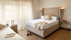 A neatly arranged hotel room with a large bed, a bedside table, a suitcase, and a chair. - Daplace - Hotel Gran Torino Suites (Rome)