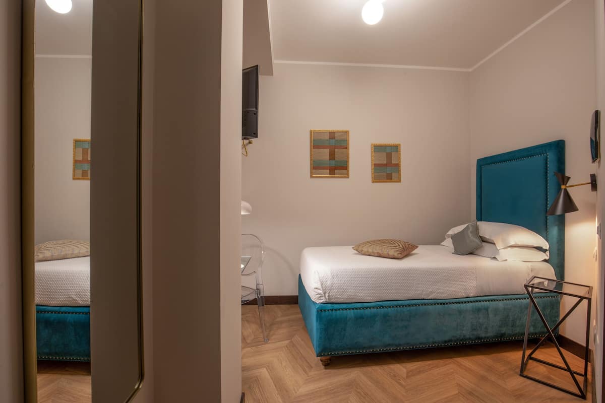 A bedroom with a teal upholstered bed, a wooden herringbone floor, and a wall-mounted TV.