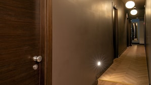 A hallway with wooden flooring, a door with a round handle, and three round ceiling lights. - Daplace - Hotel Gran Torino Suites (Rome)