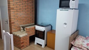 A compact kitchen with a brick oven, a small stove, a microwave, and a refrigerator. - Residencial Casa Verde (Gramado)