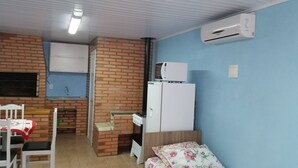 A compact room with a kitchenette, a bed, and a white air conditioner on the wall. - Residencial Casa Verde (Gramado)