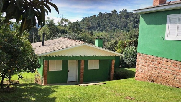 A small, single-story house with a green exterior and a white door, surrounded by a well-maintained lawn and trees. - Residencial Casa Verde (Gramado)