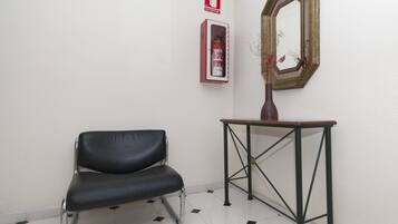 Un sillón de cuero negro, una mesita con un florero y un extintor de incendios colgado en la pared.