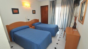 A hotel room with two beds, a desk, a chair, a TV, and a window with curtains. - Hostal Goyma I (San Fernando de Henares)