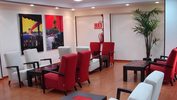 A modern waiting area with red and white chairs, black tables, and two large paintings of Parisian scenes. - Hostal Goyma I (San Fernando de Henares)
