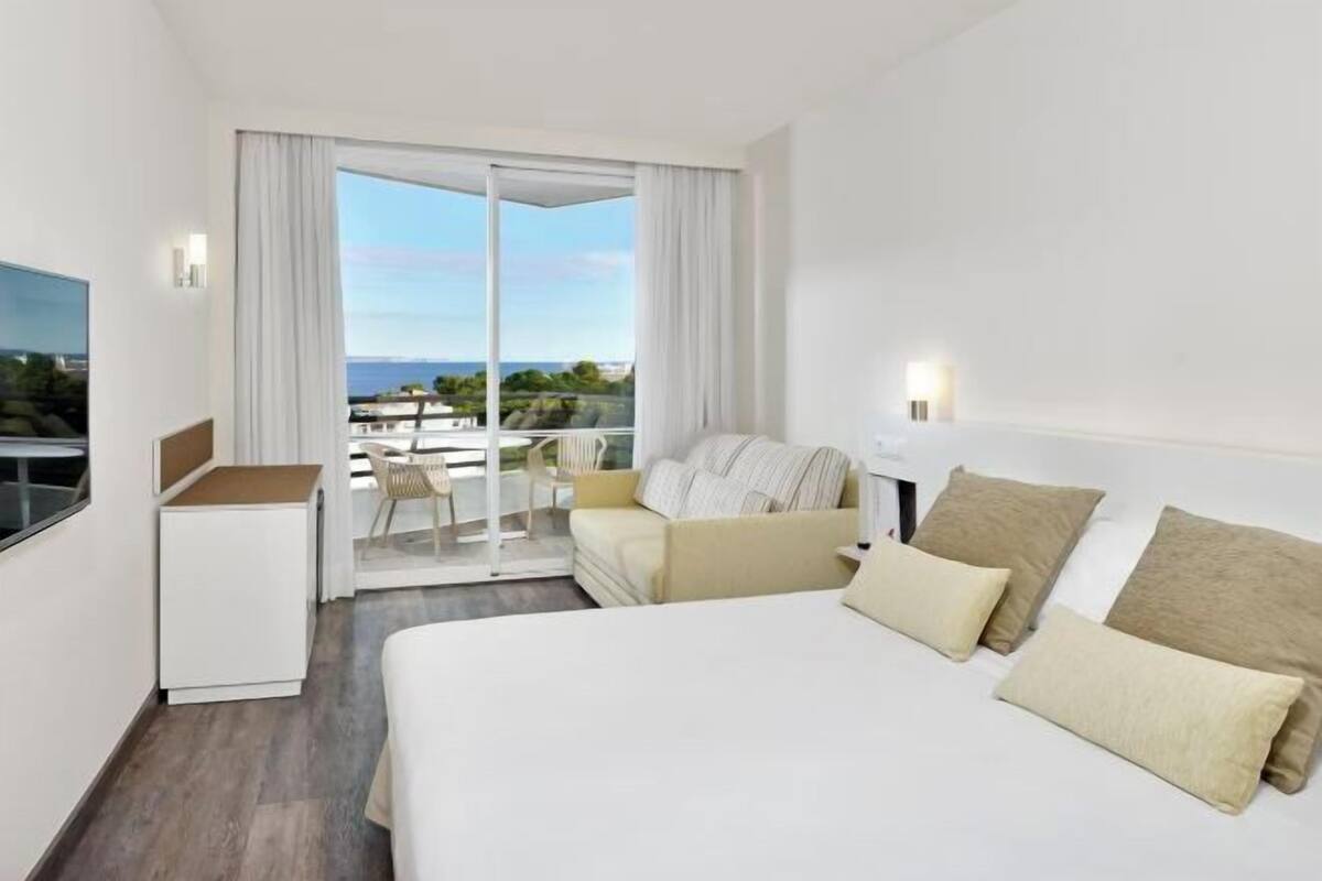 Quarto de hotel com cama, escrivaninha, cadeira e varanda com vista.
