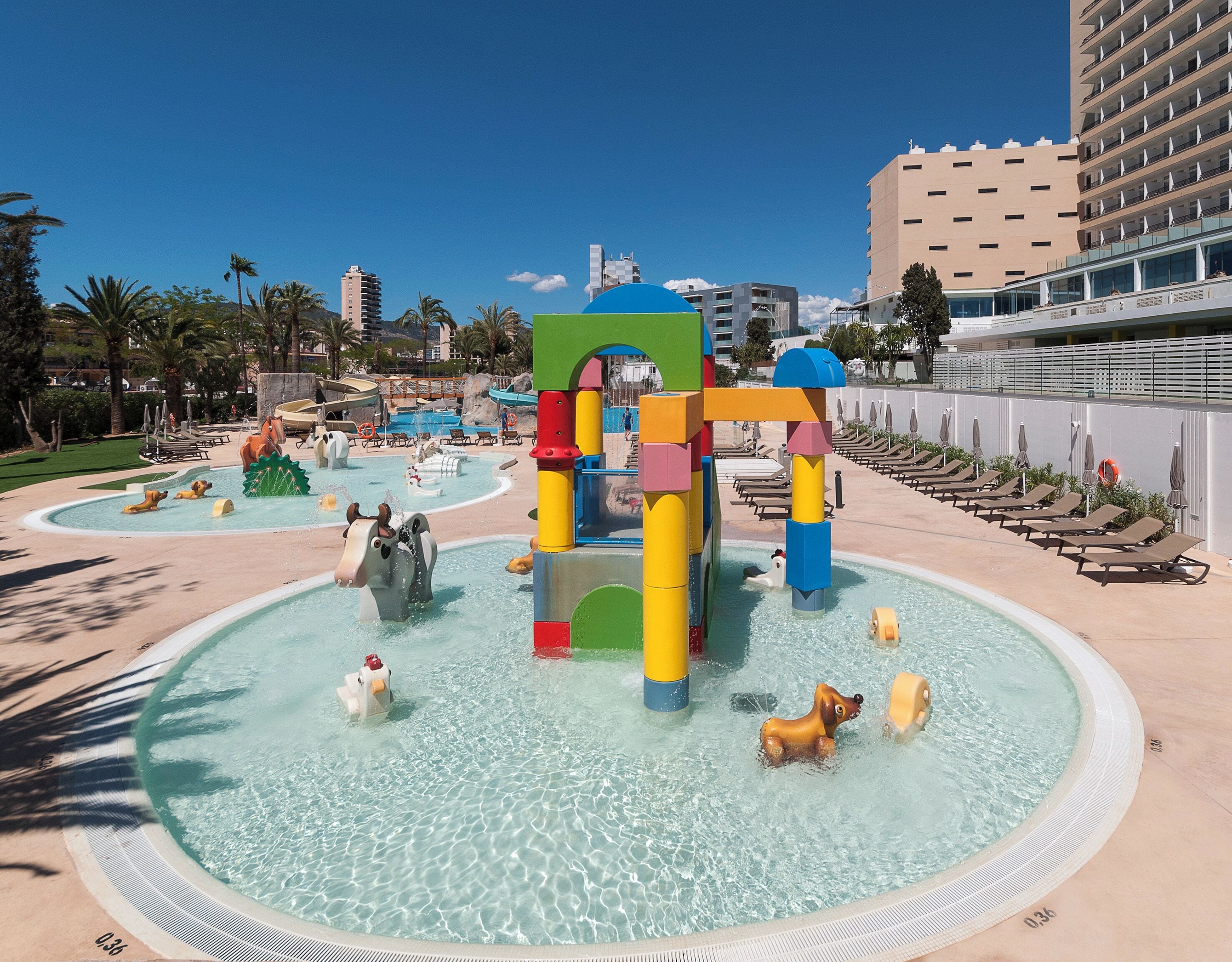 Een waterpark met een centrale speelconstructie, meerdere zwembaden en loungegedeeltes met ligbedden.