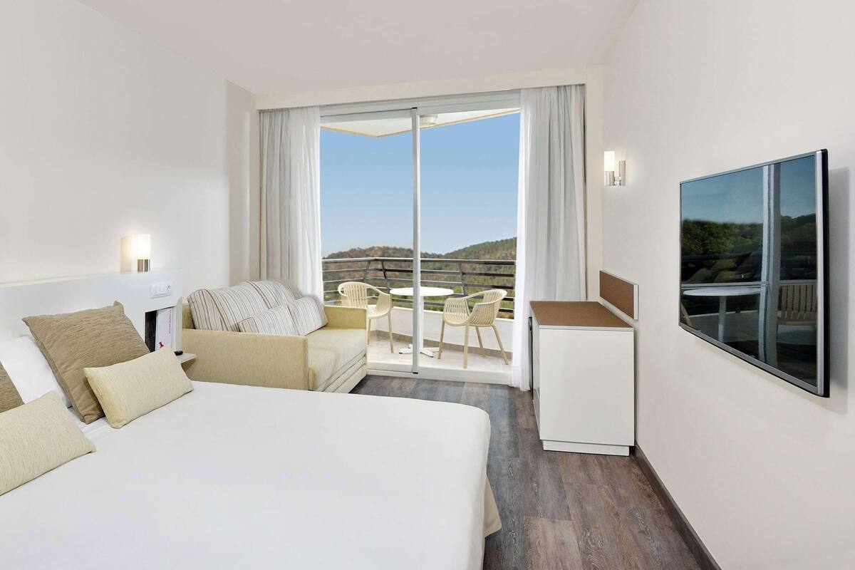 Een hotelkamer met een bed, een bureau, een stoel en een balkon met uitzicht.