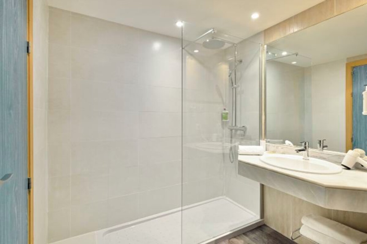A modern bathroom with a glass-enclosed shower, a large mirror, and a white sink.