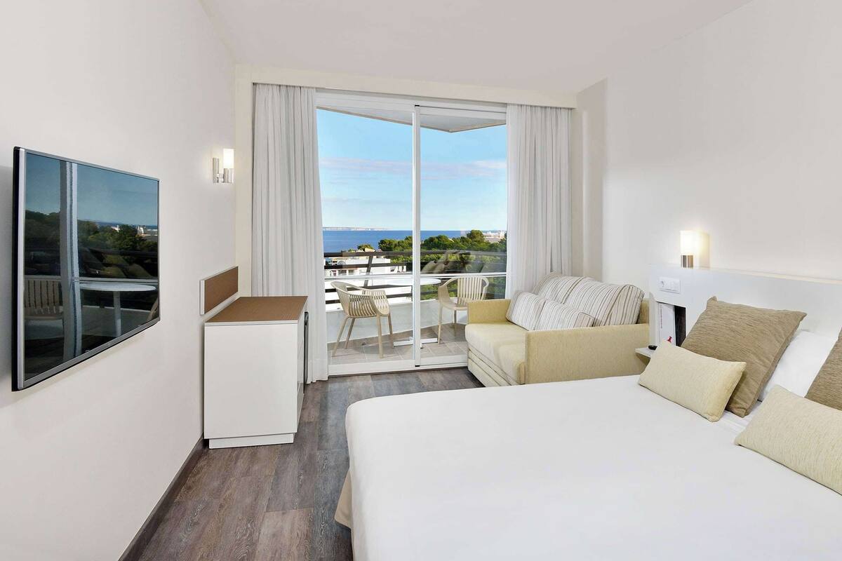 Een hotelkamer met een bed, een bureau, een stoel en een balkon met uitzicht.