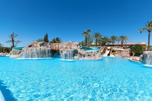 A large outdoor swimming pool with rock formations and slides, surrounded by palm trees and a clear blue sky. - Sol Barbados (Calvia)