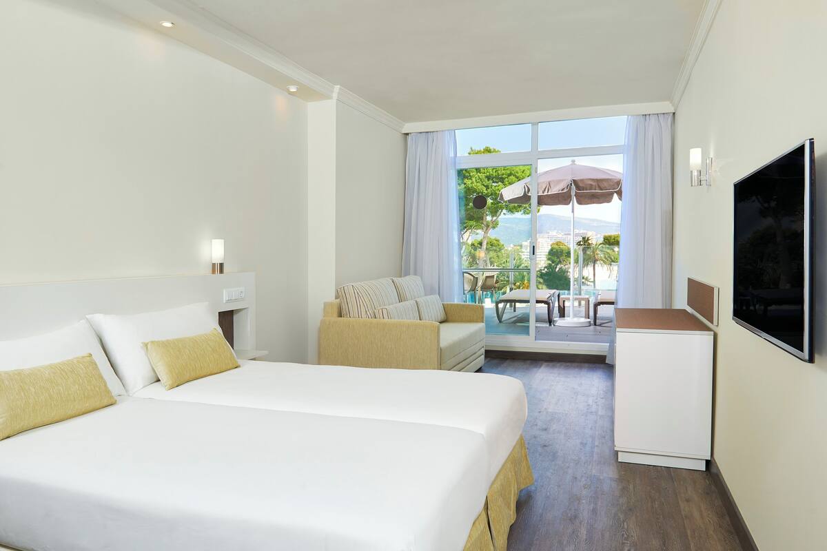 Een hotelkamer met twee bedden, een sofa, een televisie en een balkon met buitenmeubilair.