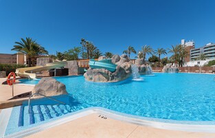 Una piscina con tobogán, palmeras y un puesto de socorristas.