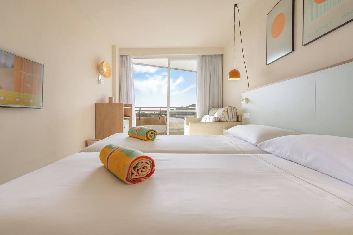 Een hotelkamer met twee bedden, een balkon en uitzicht op het landschap.