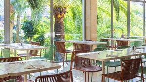 A restaurant with tables and chairs arranged for dining, large windows offering a view of palm trees.