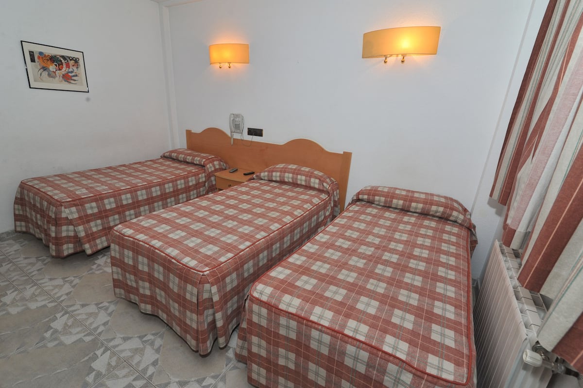 A room with three single beds, each with a checkered bedspread, a wooden headboard, and two wall-mounted lamps.