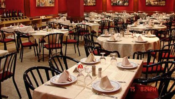 Un restaurante con varias mesas redondas, cada una con mantel blanco, platos y servilletas.