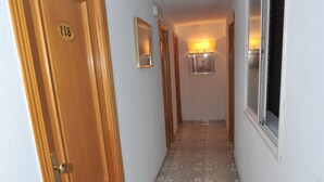 Un pasillo con una puerta de madera con el número 118, piso de baldosas y una ventana a la derecha.