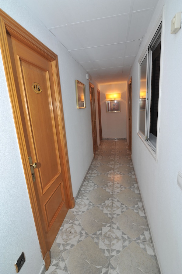 A hallway with a wooden door labeled "118," a tiled floor, and a window on the right.