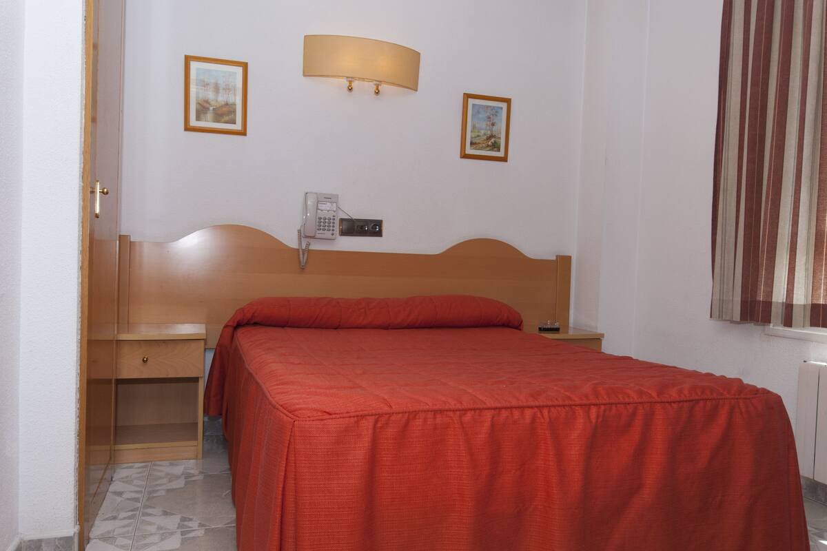 A hotel room with a bed, a bedside table, a lamp, and a telephone.