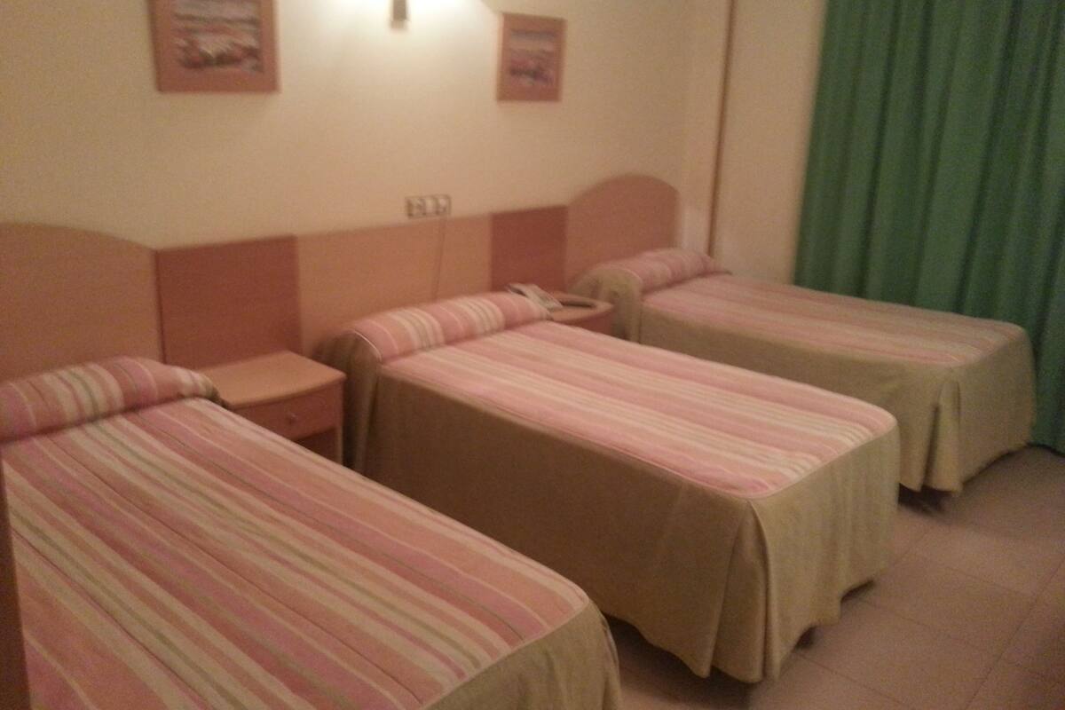 A hotel room with two single beds, a nightstand, and a wall-mounted lamp.