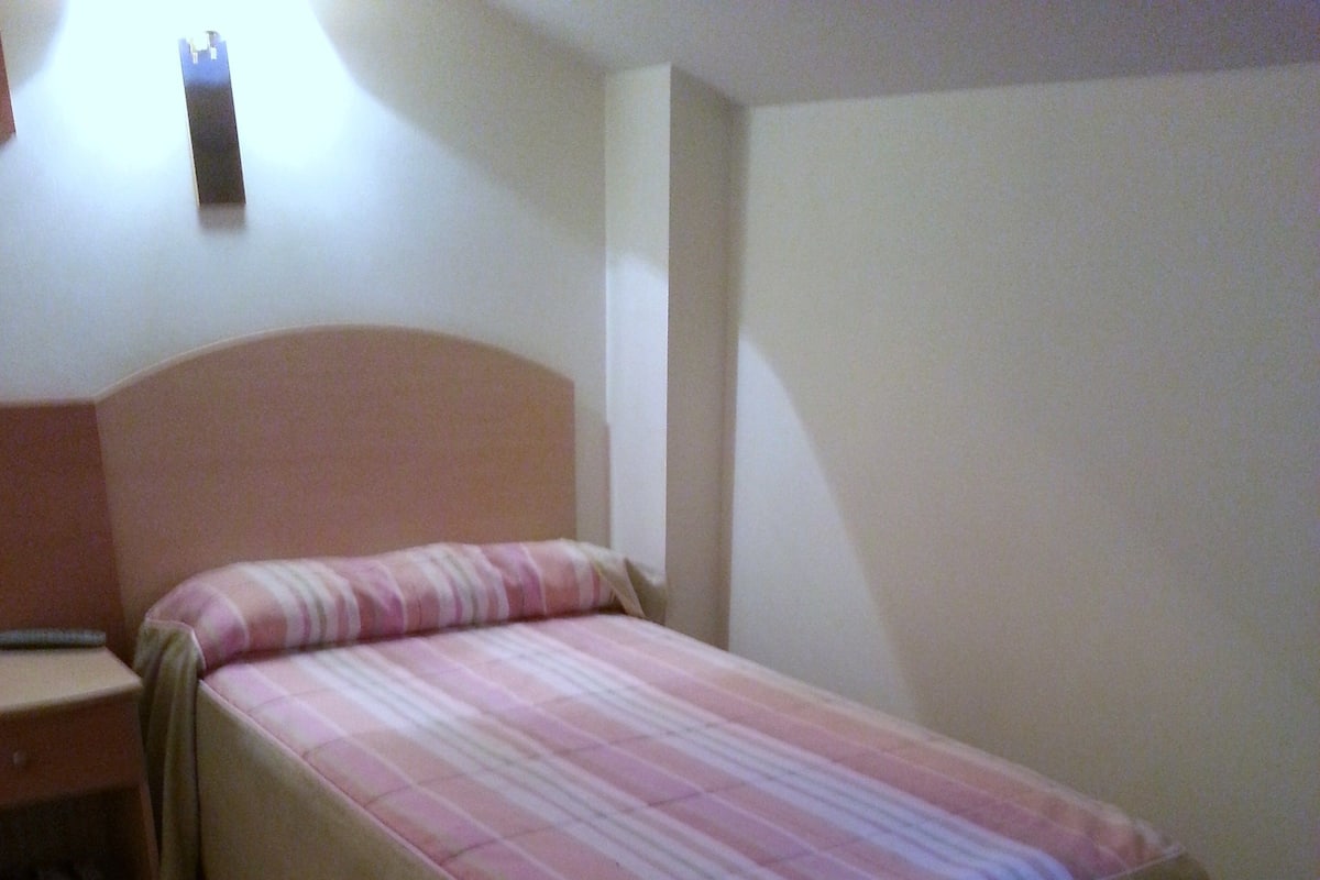 A single bed with a striped bedspread in a room with a plain wall and a nightstand.