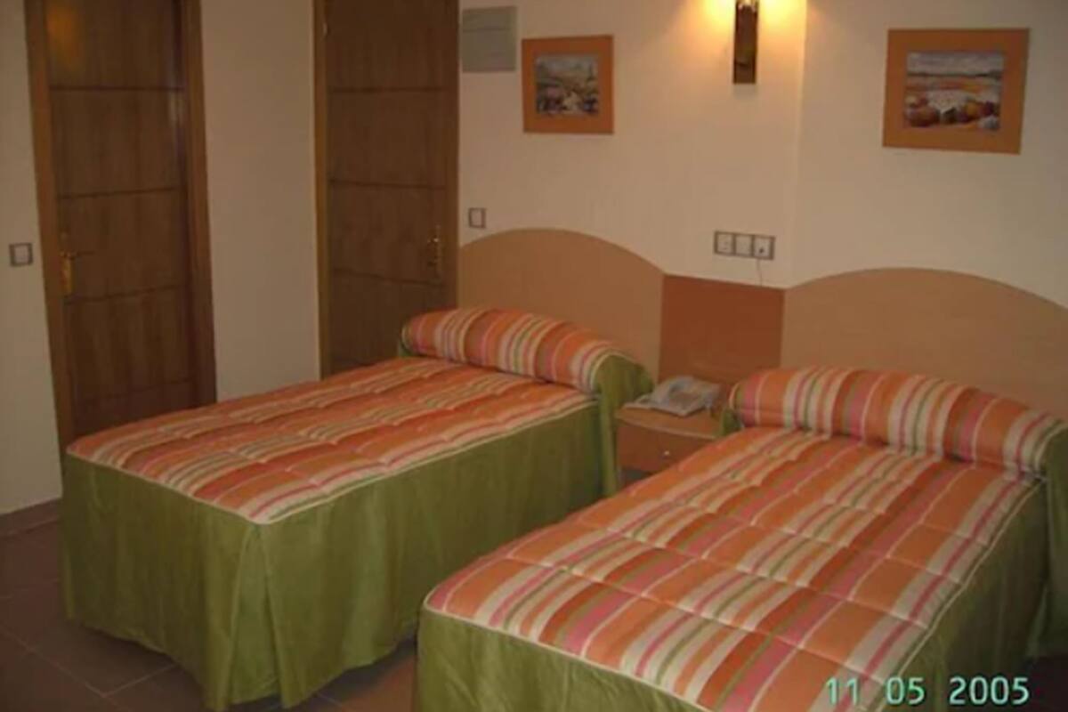 A room with two beds, each with a striped bedspread, a nightstand with a phone, and a wall-mounted lamp.
