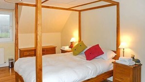Una cama con dosel, ropa de cama blanca, mesitas de noche de madera y lámparas.