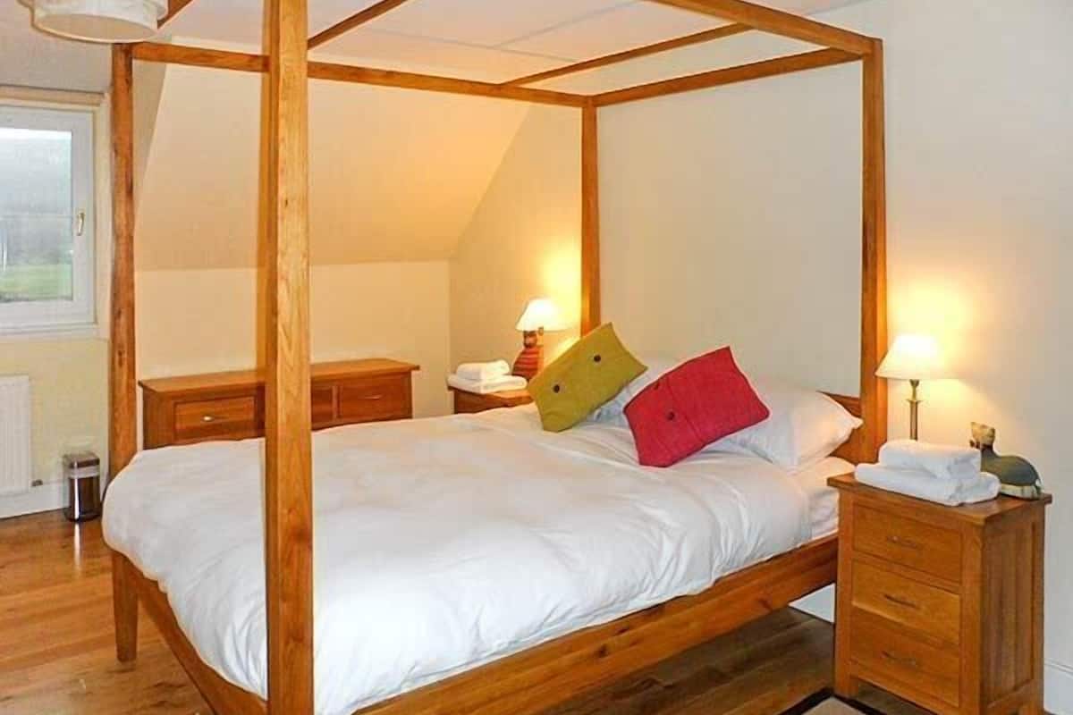 Ein Himmelbett mit weißer Bettwäsche, Holz-Nachttischen und Lampen.