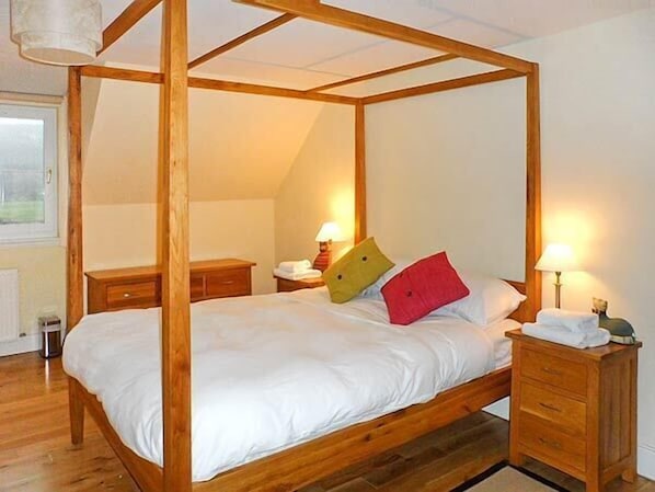 Una cama con dosel, ropa de cama blanca, mesitas de noche de madera y lámparas.