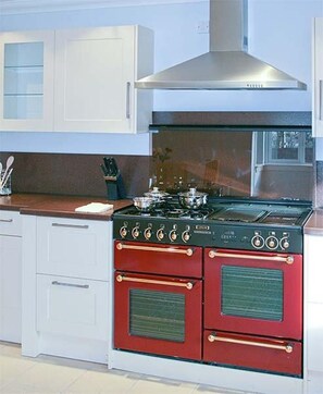 A kitchen with white cabinets, a red and black stove, and a stainless steel range hood.