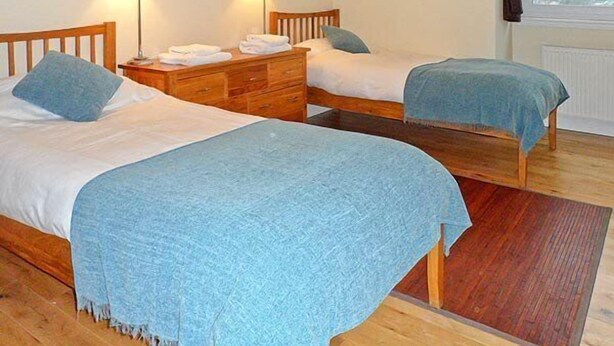 Un dormitorio con dos camas individuales, cabeceros de madera, un aparador de madera y dos lámparas de noche.