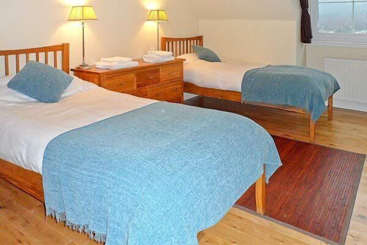 Ein Schlafzimmer mit zwei Einzelbetten, Holz-Kopfteilen, einer Holzkommode und zwei Nachttischlampen.