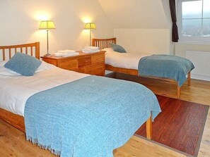 Un dormitorio con dos camas individuales, cabeceros de madera, un aparador de madera y dos lámparas de noche.