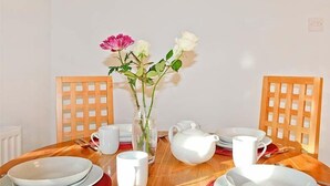 Una mesa de comedor con platos blancos, tazas y una tetera, rodeada de sillas de madera.