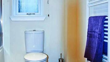 Un baño con inodoro, una ventana con cortina marrón, un radiador y una toalla colgada.
