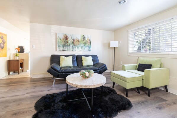 A living room with a black leather sofa, a green armchair, a round coffee table with a basket, and a black furry rug.