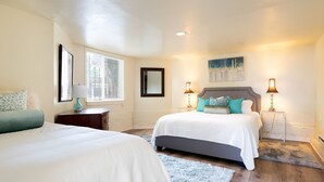 A bedroom with two beds, a nightstand, a lamp, a window with blinds, and a painting on the wall. - Bright & Spacious One Bedroom Apartment (Oakland)