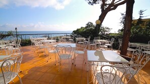 An outdoor terrace with white metal tables and chairs, a tiled floor, and a view of the sea. - Grand Hotel Ischia Lido (Ischia)